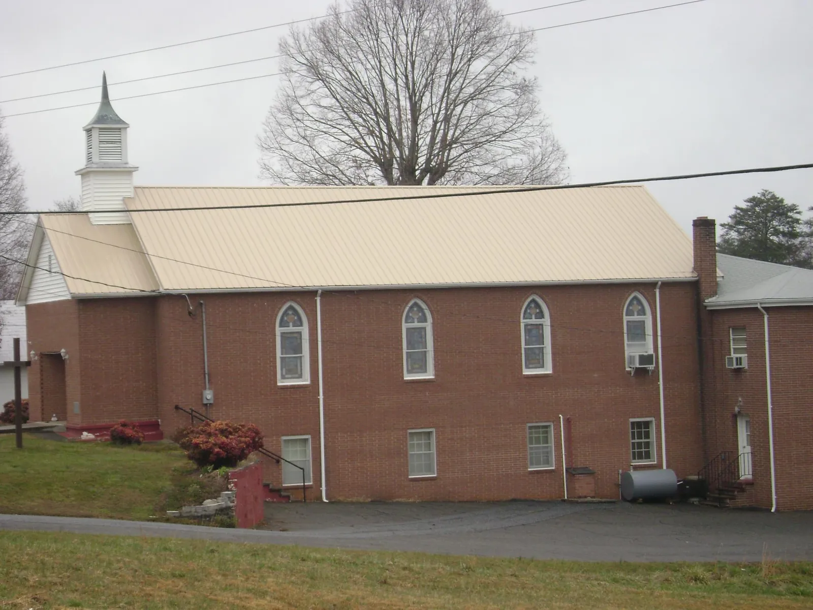 New tan metal roof on a brick church with a white steeple in Mechanicsville